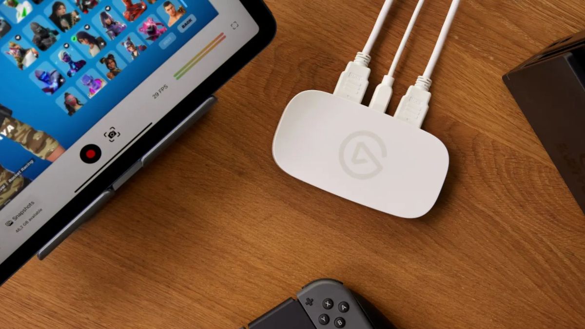 Elgato Game Capture Neo capture card in white kept on a table next to an iPad and other accessories.